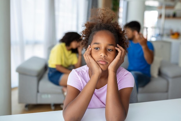 Sad girl listening to her parents arguing in living room at home