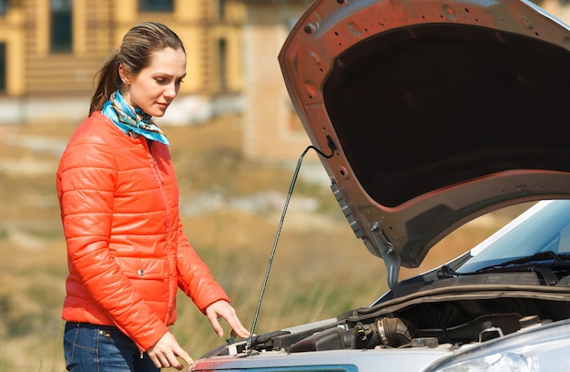 Sad girl looking at a broken down car with the hood open