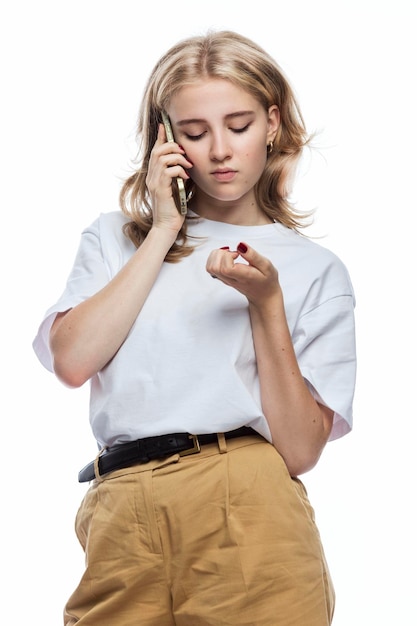 Sad girl speaks on the phone A teenager in beige trousers and a white Tshirt Frustration and bad news White background Vertical