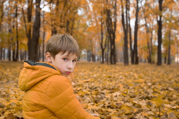 Sad little boy in the autumn park A child on a walk on a cloudy rainy day