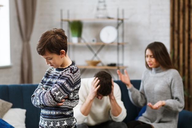 Sad little boy feels upset while his parents fighting at background. Mother and father quarrel. Family conflicts and divorce lead to children's psychological problem. Children's mental disorders.