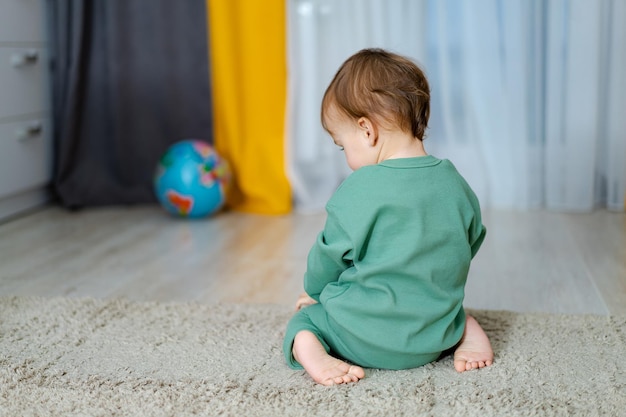 Sad little boy sitting in the room Lonely moody sulking boy Boy turned his back Offenced little child