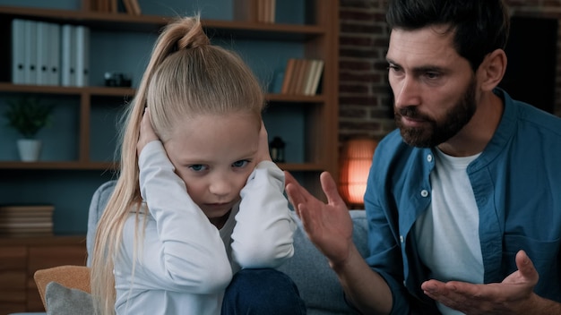 Sad little daughter feel stress cover ears ignoring scream angry annoyed dad shouting on girl