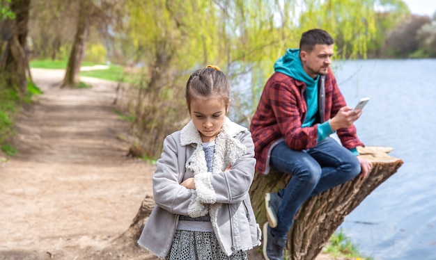 Sad little girl because dad checks his phone while walking in the woods and pays no attention to her.