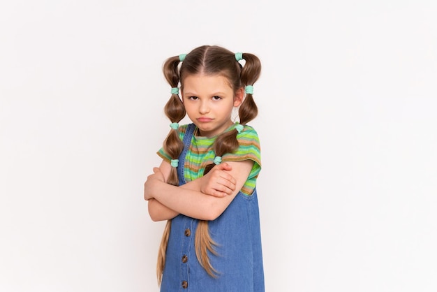 A sad little girl in a denim sundress on a white isolated background A frustrated child