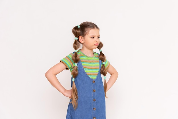 A sad little girl in a denim sundress on a white isolated background A frustrated child