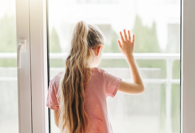 Sad little girl looking through window at home