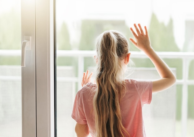 Sad little girl looking through window at home