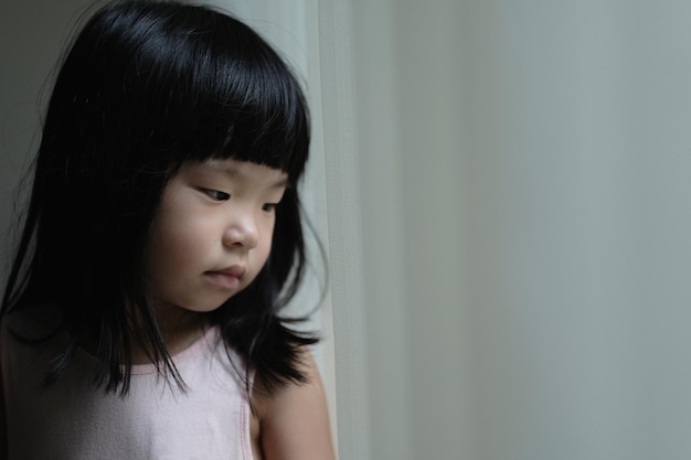 Sad lonely little girl standing beside a window