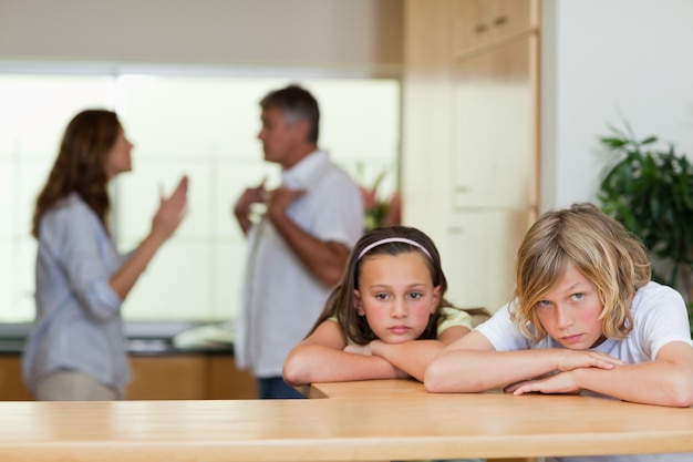 Sad looking siblings with arguing parents behind them