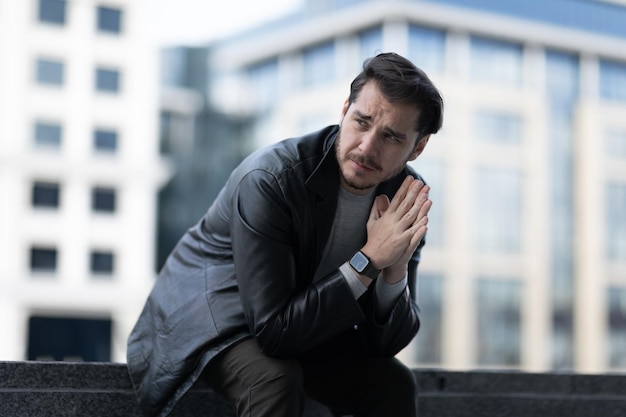 A sad man with a sad expression folded his hands in prayer sitting in the city on the steps