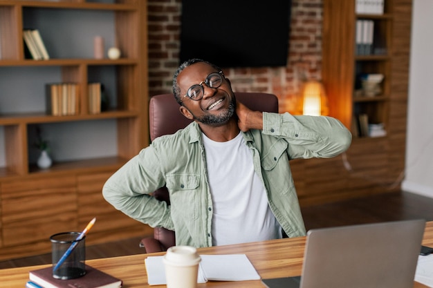 Sad mature african american male manager in glasses casual suffers from back and neck pain from stress