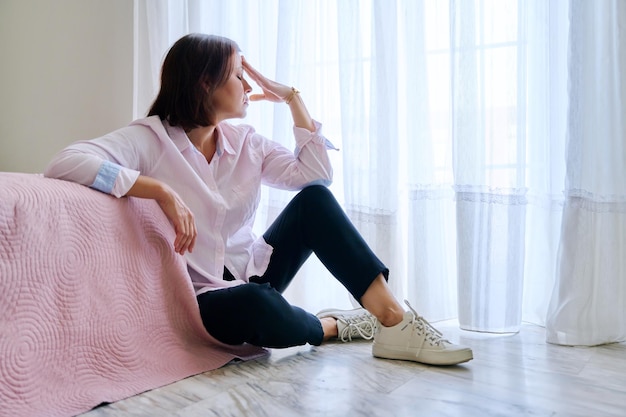 Sad middle aged depressed woman sitting on the floor in the bedroom