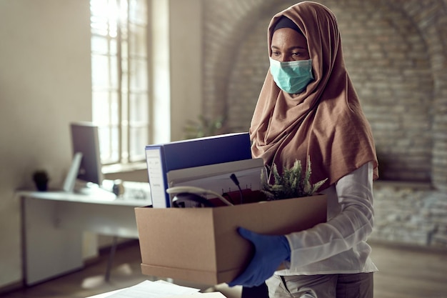 Sad Muslim businesswoman carrying her belongings and leaving the office after being fired due to coronavirus epidemic