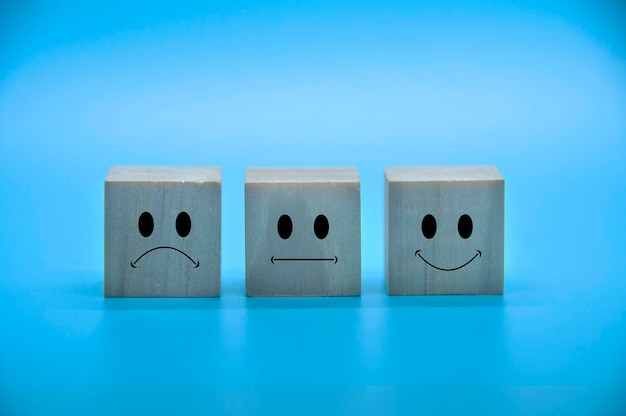 Sad neutral and happy emoticon faces on wooden cubes with blue background cover Customer satisfaction and evaluation concept