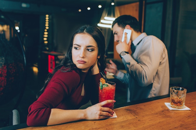 Sad picture of girl looking to the right. She is sad because man is answering to the phone call and not spending time with her. She doesn't have a good mood.