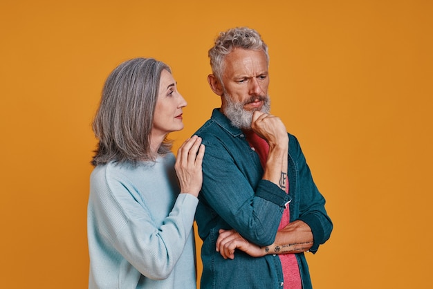 sad senior couple standing together against orange background