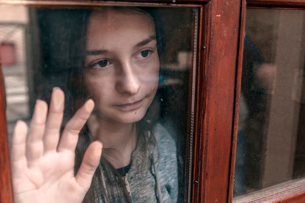 Sad teenage girl looking out the window on a cold autumn day