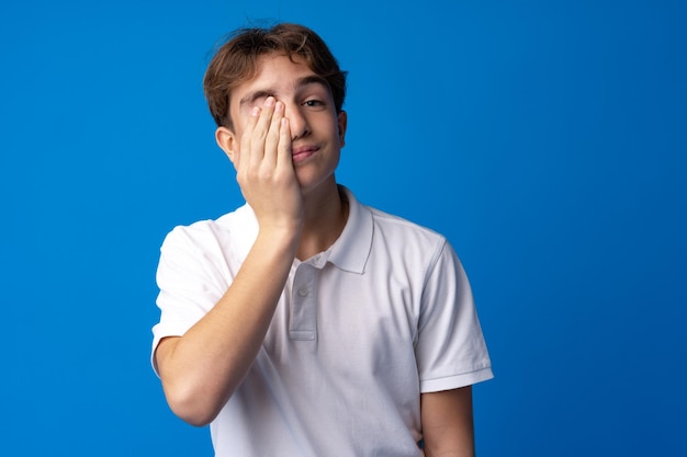 Sad teenager boy failed touching face against blue background