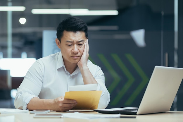 Sad over thinking asian businessman reading bad news letter from bank