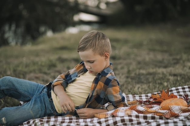 Sad thinking dreaming kid boy lies on a blanket near a river or lake