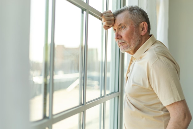 Sad tired lonely disappointed older senior man at home alone unhappy grandfather looking sadly outsi