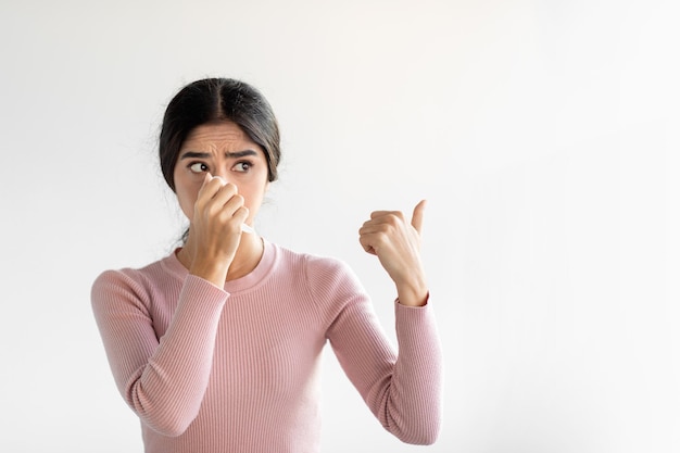 Sad upset funny young hindu female suffering from cold blows nose in napkin on gray wall background