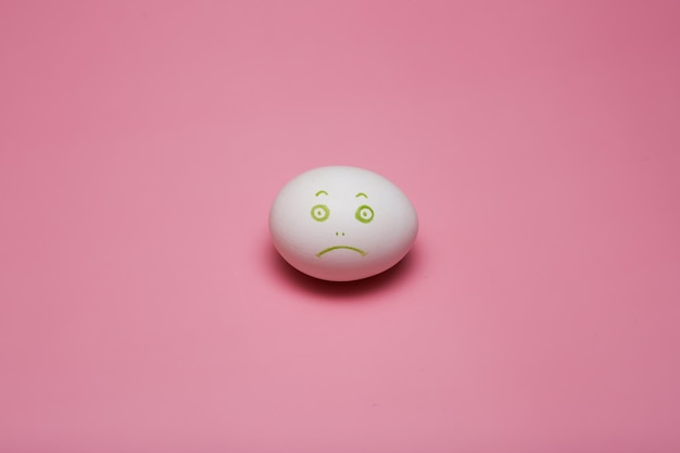 Sad white egg emoticon painted face. Easter. On a pink background. High quality photo