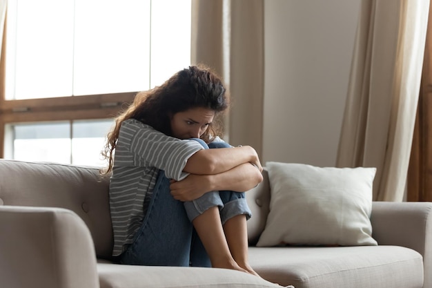 Photo sad woman hug knees sit on couch feels lonely goes through divorce or break up female with drug or alcohol addiction problem need rehab help unplanned pregnancy made decision about abortion concept