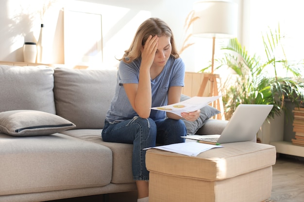 Sad woman with the bills sitting on a sofa in the living room.