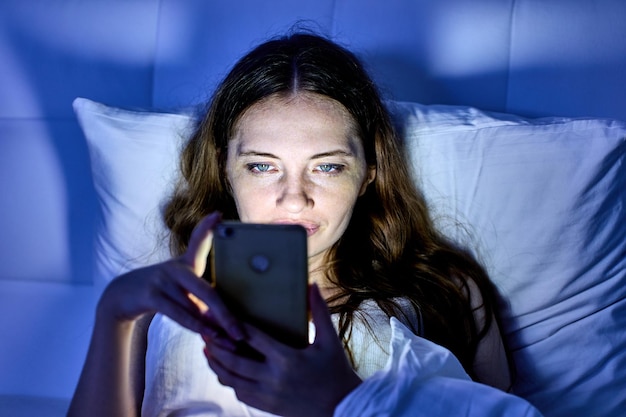 Sad woman with handy is lying in bed and watching video