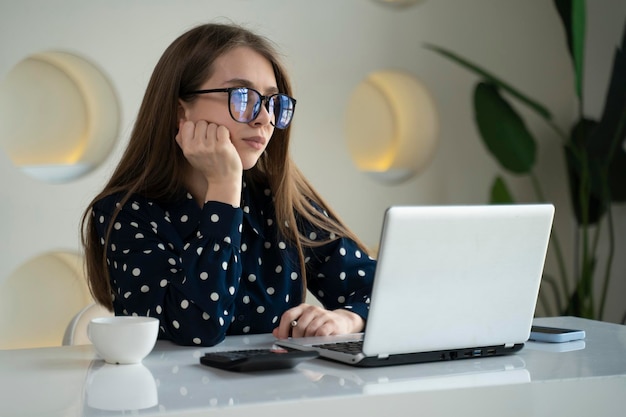 A sad woman works in an office a business woman is bored looking at a laptop screen