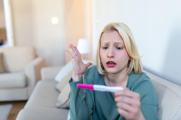 Sad worried woman checking her recent pregnancy test sitting on couch at home Maternity child birth and family problems concept unwanted pregnancy