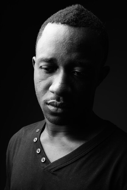 Sad young African man against black wall in black and white