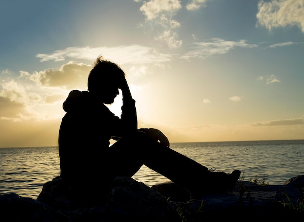 Sad young man silhouette worried on the stone at sunset ,Silhouette concept