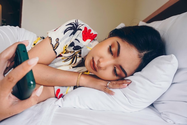 Sad young woman frowning from the bed waiting for a call while holding the smartphone