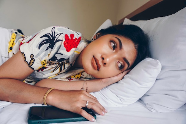 Sad young woman frowning from the bed waiting for a call while holding the smartphone