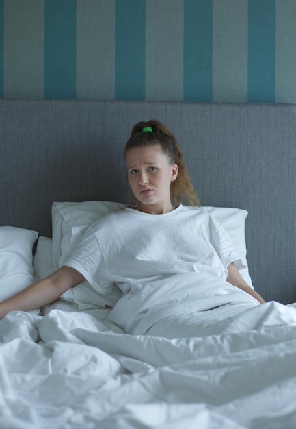 Sad young woman lying in bed alone looking to aside at an empty pillow depressed feeling lonely