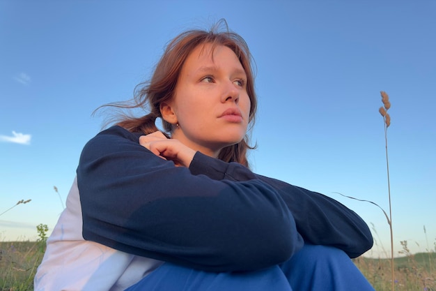 Sad young woman sitting alone in a field sunset in summer weather