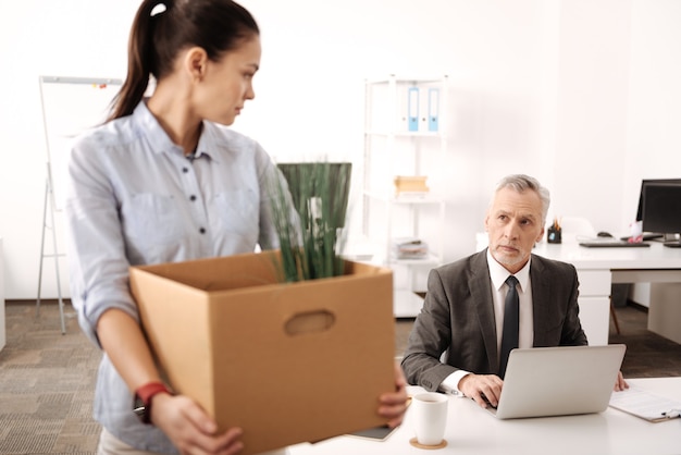 Sad young woman standing in profile holding big box while looking aside