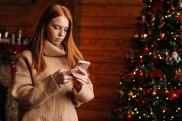 Sad young woman typing message on mobile phone while selfisolating during the winter holiday