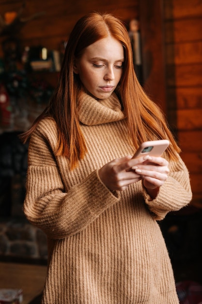 Sad young woman typing message on mobile phone while selfisolating during the winter holidays