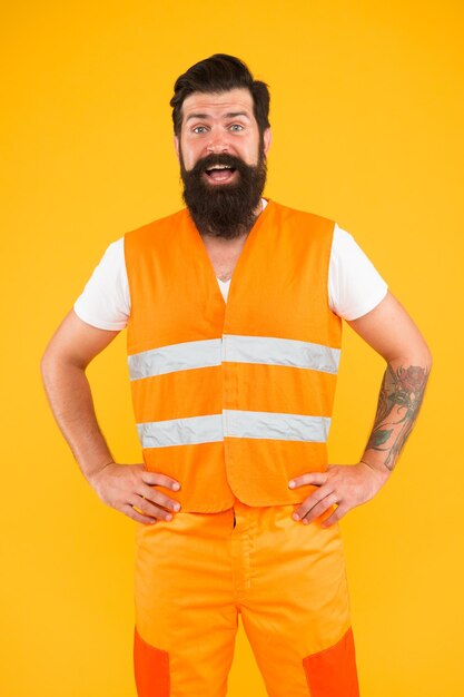 Photo safety apparel for construction industry bearded brutal hipster safety engineer high visibility reflective safety vest man worker protective uniform orange background safety equipment concept