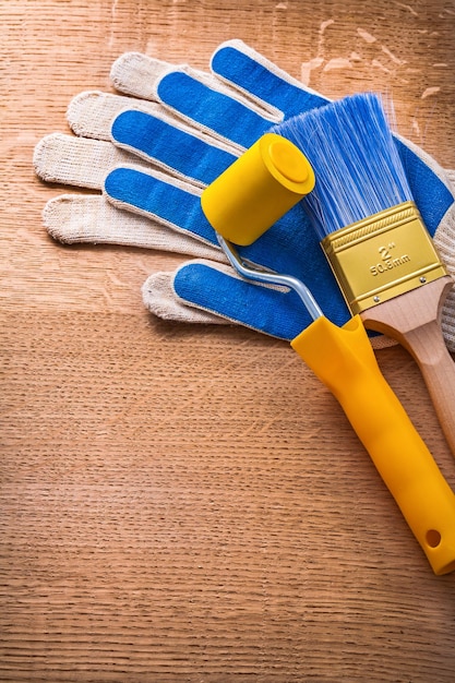 Safety gloves with paint roller and brush on wooden board construction concept