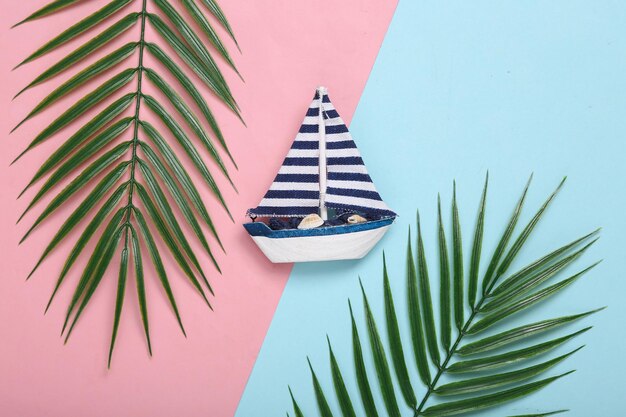 Saiboat and palm leaves on pink blue background Tropical composition Top view Flat lay