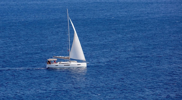 Sailboat with white sail in blue Aegean sea background Summer holiday in Greece Cyclades island