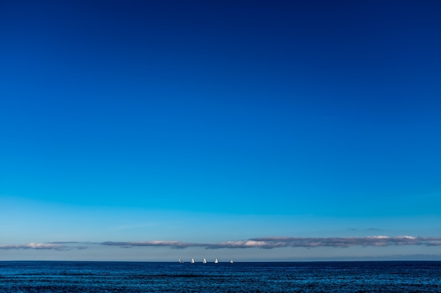 Sailboats on the horizon line on the sea, looking at view from the beach of Barcelona