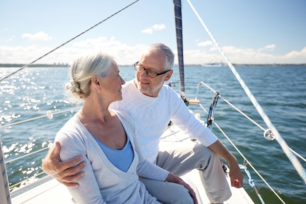 sailing, age, tourism, travel and people concept - happy senior couple hugging on sail boat or yacht deck floating in sea