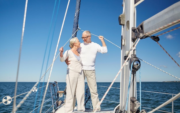 sailing, age, tourism, travel and people concept - happy senior couple hugging and talking on sail boat or yacht deck floating in sea