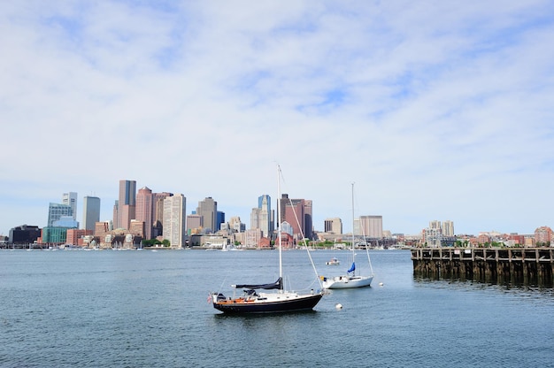 Photo sailing boat rest with dock in bay and boston downtown skyline with urban skyscrapers over sea in the morning.